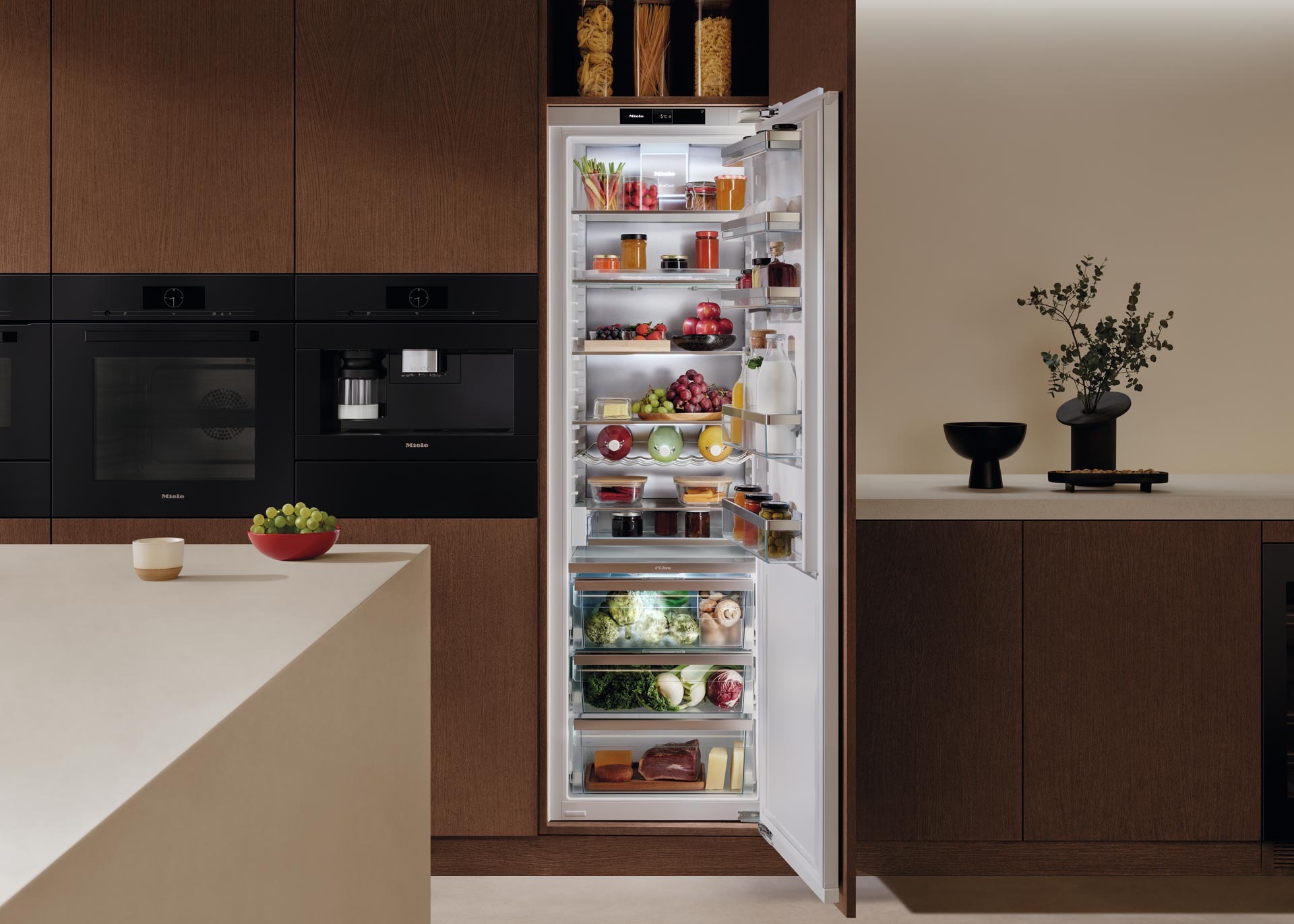 Cocina con un refrigerador de puerta abierta, horno y cafetera empotrados a un lado.